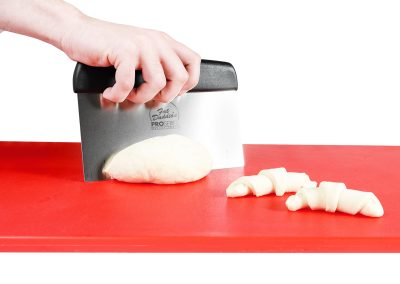 Baker with a Bench Scraper Dough Cutter on a cutting board with dough in a bakery