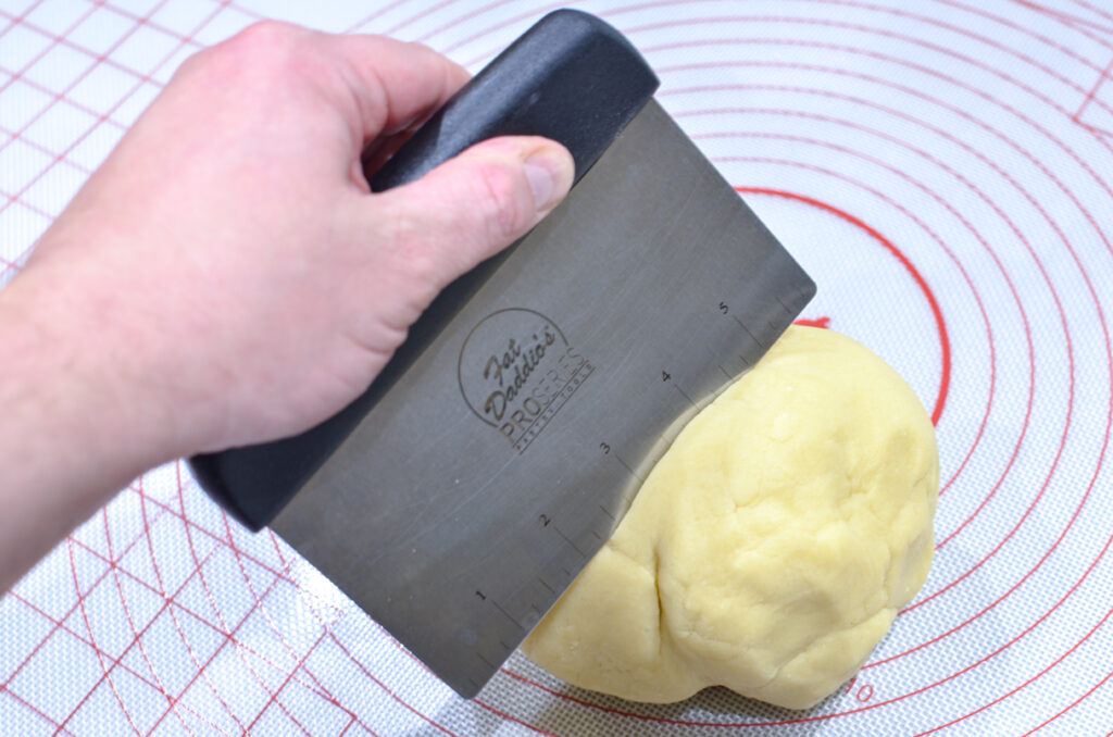 A baker pushing a Bench Scraper into dough on a baking mat