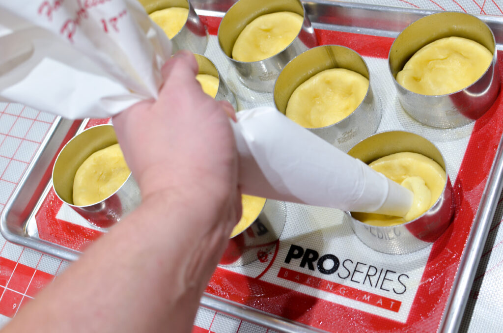 A baker piping pastry cream onto pastry rings with Torta Della Nonna dough on a work mat