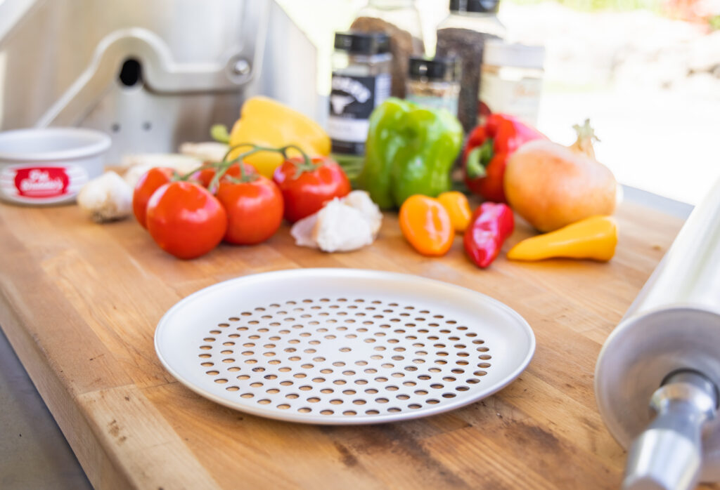 a pizza pan next to vegetables and a BBQ grill